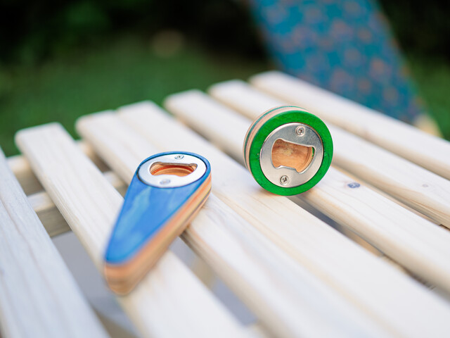 Auf einem Gartentischchen aus Holz liegen zwei, aus Holz gefertigte und bunt bemalte Flaschenöffner.