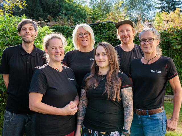 Sechs Personen stehen in einem grünen Garten zu einem Gruppenfoto zusammen.