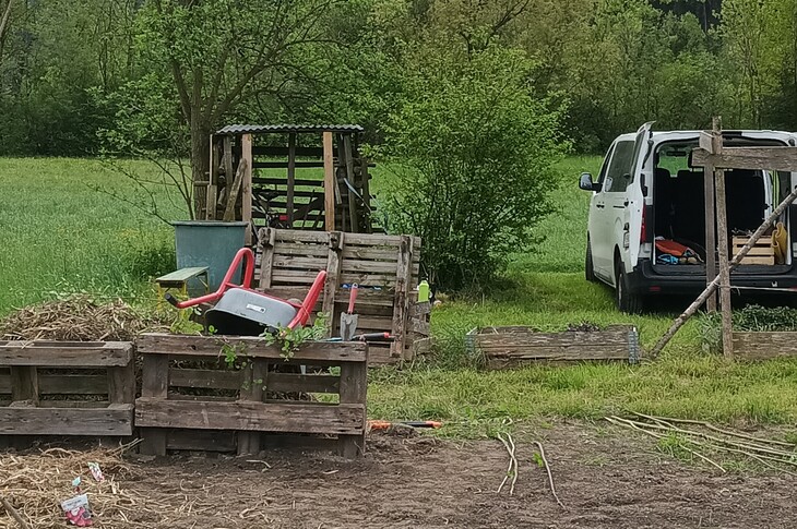 Eine Personen steht neben einem Hochbeet aus Holz auf einem brachliegenden Feld.
