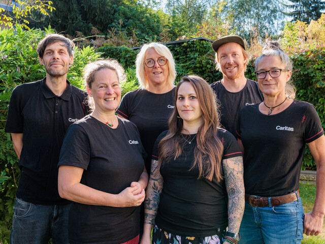 Sechs Personen stehen in einem grünen Garten zu einem Gruppenfoto zusammen.