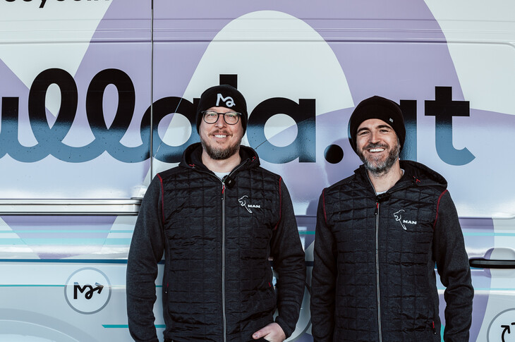 Abholservice für Recyclingstoffe Zwei Männer in schwarzer Merchandise-Kleidung stehen vor einem Transporter mit der Aufschrift „Mullala.at".
