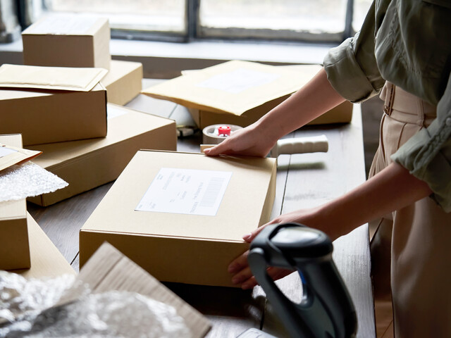 Weibliche Lagerarbeiterin bereitet eine Paketbox für den Versand vor.